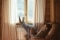 The picture shows a man with a book in his hands, sitting on an armchair in front of a window with his legs on a radiator.