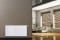 Vitoset universal radiator, living room in the background with shaded windows, sofa, plants and yucca palms..